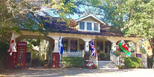 Charming house with a porch, flags from various countries, and a red telephone booth in a lush, green setting.