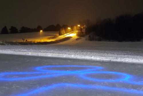 A snowy landscape at night with glowing blue patterns on the ice and a lit path in the background.