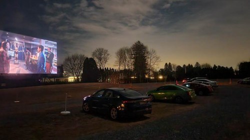 A drive-in theater at night, featuring a large screen and parked cars under a starry sky.