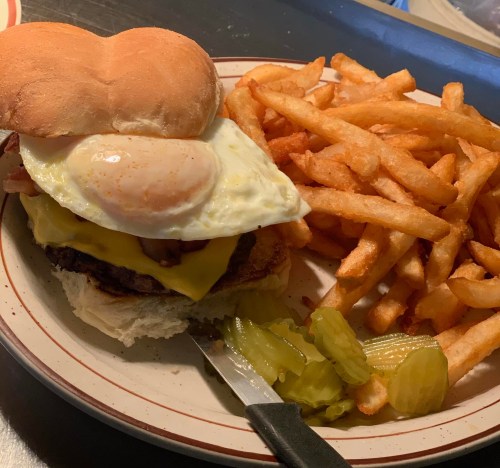 A plate with a cheeseburger topped with a fried egg, pickles, and a side of crispy French fries.