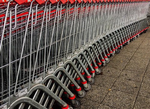 A row of neatly aligned shopping carts with red handles on a paved surface.