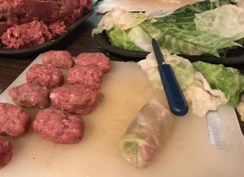 Ground meat and lettuce leaves on a cutting board, with a knife and a partially rolled lettuce wrap.