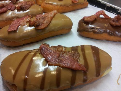 A close-up of donuts topped with chocolate and caramel icing, garnished with crispy bacon pieces.