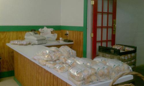 A small store interior with a cash register and bags of bread on the counter, surrounded by wooden walls and green accents.