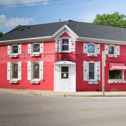 A bright red building with white shutters and stained glass windows, featuring an "Open" sign.