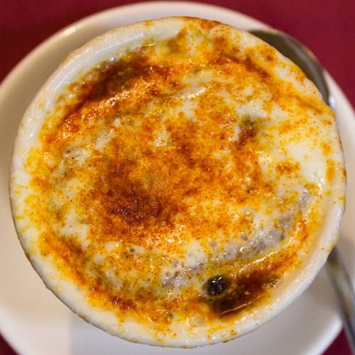 A creamy dish topped with a golden-brown crust and sprinkled with spices, served in a white bowl on a plate.