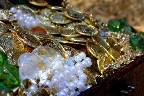 A treasure chest filled with gold coins, sparkling gems, and strands of pearls, glistening in the light.