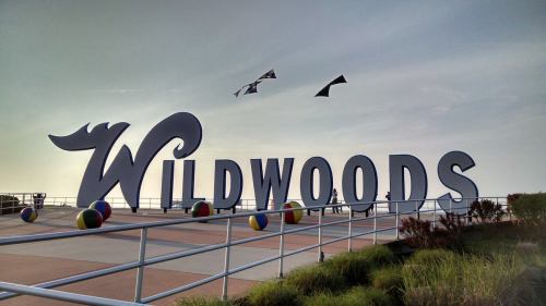 Large "Wildwoods" sign with colorful beach balls and kites flying in the background against a clear sky.