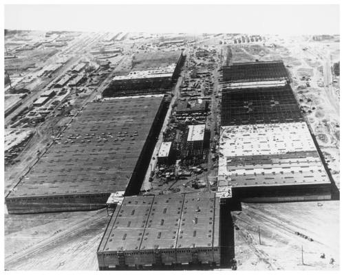 Aerial view of a large industrial complex with multiple buildings and construction areas, in black and white.