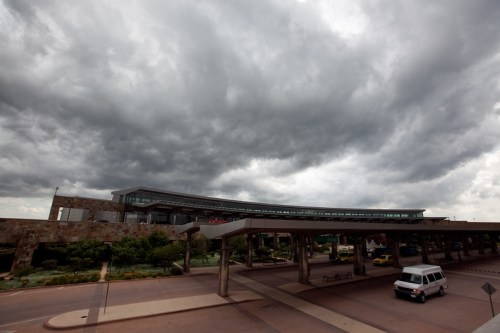A modern airport building under a dramatic sky filled with dark, ominous clouds.