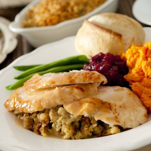 A plate featuring sliced turkey with gravy, stuffing, green beans, cranberry sauce, sweet potatoes, and a roll.