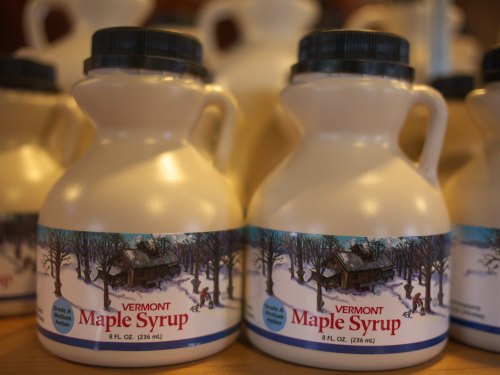 Bottles of Vermont maple syrup with a winter scene label, arranged closely together on a shelf.