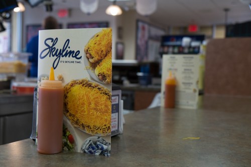 A menu featuring Skyline chili with a bottle of sauce on a table in a casual dining setting.