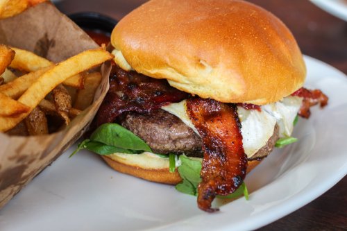 A juicy burger with bacon, lettuce, and cheese, served with a side of crispy fries on a white plate.