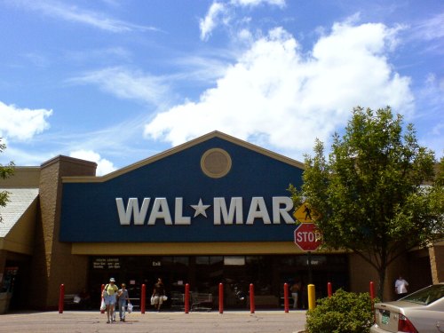 Exterior of a Walmart store with a blue sign, red poles, and a clear sky in the background.