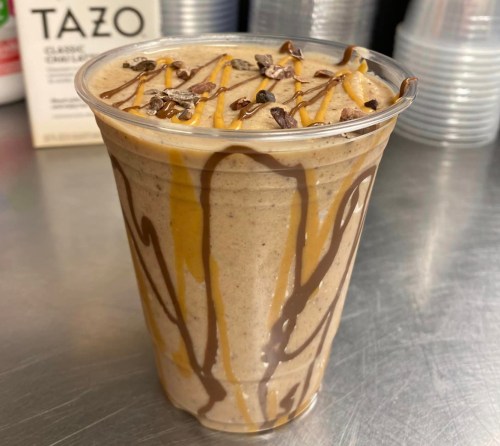 A creamy beverage in a clear cup, topped with chocolate drizzle and caramel, with a sprinkle of chocolate bits.