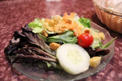 A fresh salad with mixed greens, cucumber slices, a cherry tomato, and croutons on a glass plate.