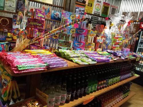 A colorful display of various candies and sodas on wooden shelves in a vintage-style store.