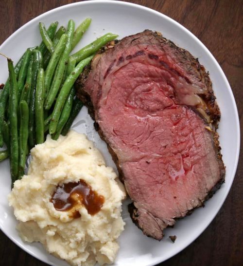A plate with sliced prime rib, creamy mashed potatoes with gravy, and steamed green beans.