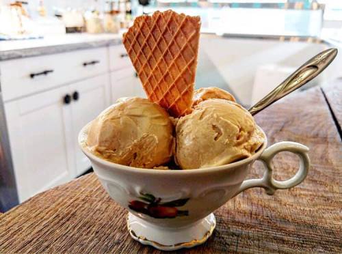A bowl of creamy ice cream scoops with a waffle cone, placed on a wooden table.