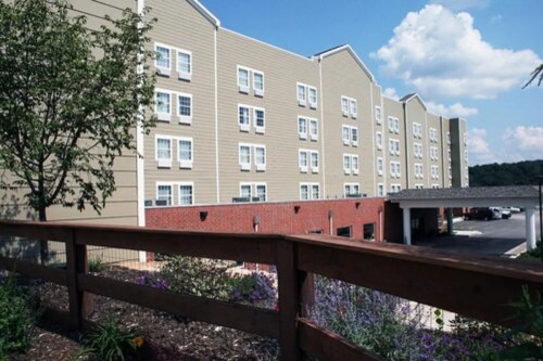 A multi-story hotel building with a mix of brick and siding, surrounded by greenery and blue skies.