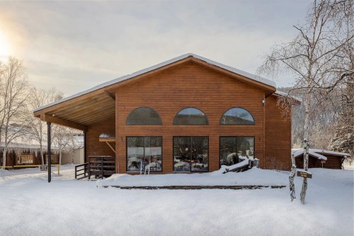 A wooden building with large arched windows, surrounded by snow and trees, under a cloudy sky.