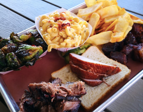 A metal tray filled with smoked meats, macaroni and cheese, Brussels sprouts, fries, and slices of bread.