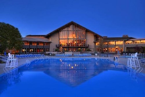 A serene pool area at dusk, featuring lounge chairs and a modern building with large windows in the background.