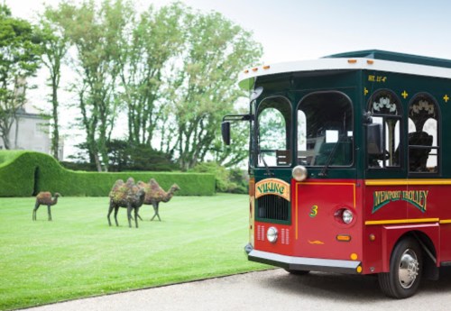 A colorful trolley parked on a lawn with whimsical camel sculptures in the background and lush greenery.