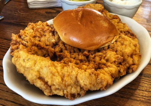 A plate of crispy fried chicken with a soft bun, served on a wooden table.