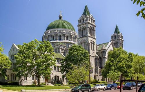 Historic building with a green dome and towers, surrounded by trees and clear blue sky.