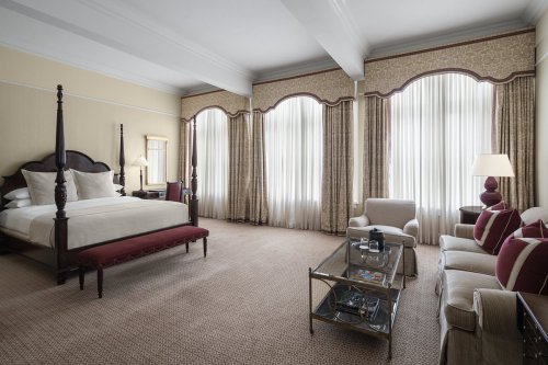 A spacious hotel room featuring a king bed, elegant curtains, a seating area, and a glass coffee table.