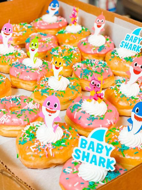 A box of colorful donuts topped with frosting, sprinkles, and cute Baby Shark character decorations.
