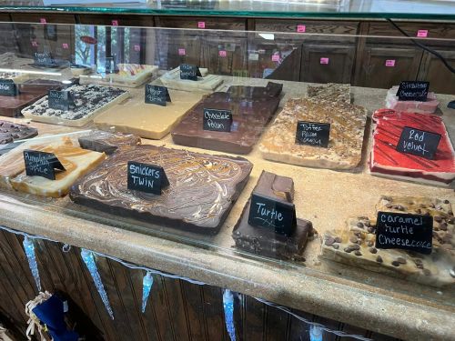 A display case filled with various fudge flavors, each labeled with small black signs.