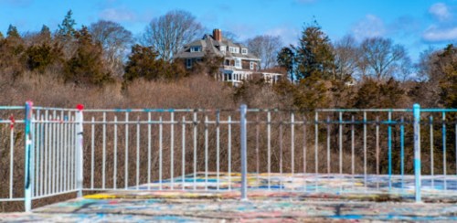 A distant house surrounded by trees, viewed from a colorful, graffiti-covered platform with a railing in the foreground.