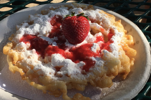 A plate of funnel cake topped with powdered sugar, strawberry sauce, and a fresh strawberry in the center.