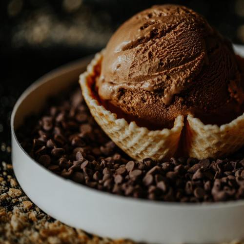 A scoop of chocolate ice cream in a waffle cone bowl, surrounded by chocolate chips on a dark background.