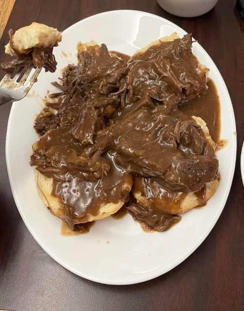 A plate of biscuits topped with tender beef and rich brown gravy, with a fork holding a piece of meat.