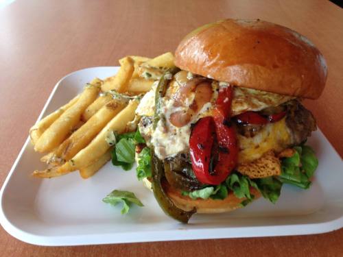 A juicy burger with grilled peppers, lettuce, and a fried egg, served with a side of crispy fries on a white plate.