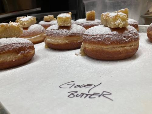 A tray of powdered donuts topped with gooey butter squares, labeled "Gooey Butter."