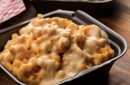 A close-up of creamy macaroni and cheese in a black takeout container.