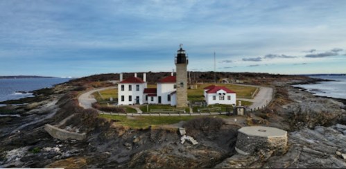 A scenic view of a lighthouse on a rocky shore, surrounded by grassy land and a calm sea under a cloudy sky.