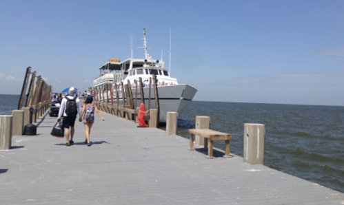 A boat docked at a wooden pier with people walking along it under a clear blue sky.
