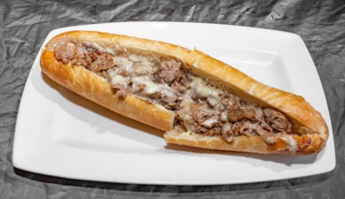 A toasted sub sandwich filled with seasoned beef and melted cheese, served on a white plate.