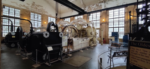 Historic industrial machinery displayed in a large, well-lit room with large windows and exposed brick walls.
