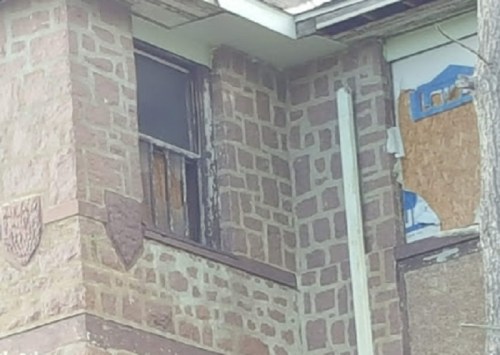Close-up of a weathered brick building with boarded windows and peeling paint, showing signs of neglect.