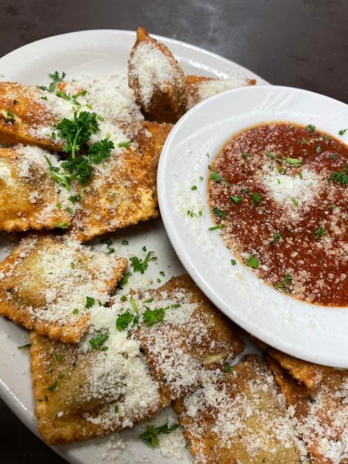 A plate of golden-brown ravioli topped with grated cheese and parsley, served with a side of marinara sauce.
