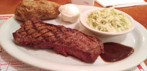 A plate with a grilled steak, baked potato with sour cream, and a side of coleslaw.