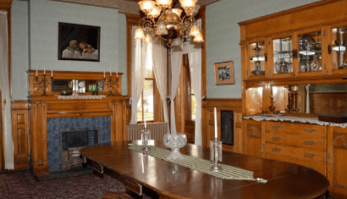 Elegant dining room featuring a wooden table, chandelier, and vintage decor, with a fireplace and glass display cabinet.