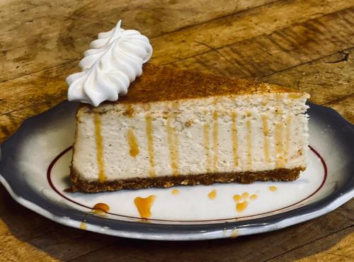 A slice of cheesecake with a graham cracker crust, topped with whipped cream and drizzled with caramel sauce.